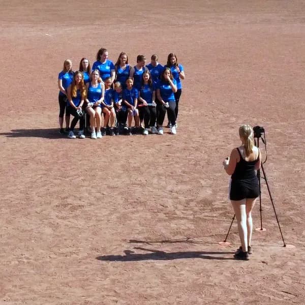 Gruppe der TSG Irlich in blauen Trikots posiert für ein Mannschaftsfoto auf dem Spielfeld, während eine Fotografin in schwarzem Kleid mit Kamera auf Stativ das Foto macht.
