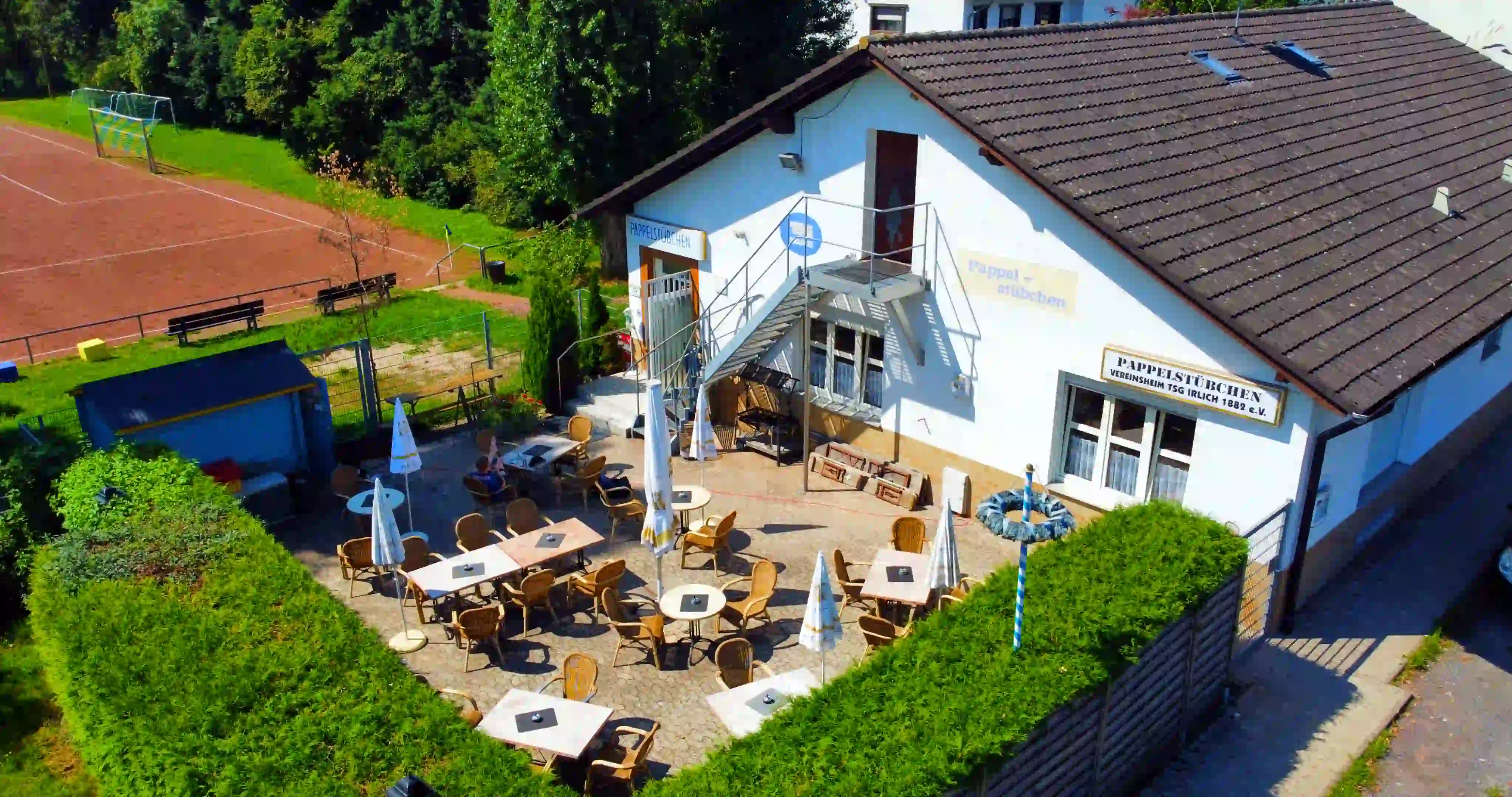 Das Bild zeigt einen modernen Arbeitsplatz. Im Vordergrund steht ein MacBook Pro mit einem ausgeschalteten Bildschirm auf einem schwarzen Schreibtisch. Rechts daneben befindet sich ein Festnetztelefon und eine kabellose Maus. Im Hintergrund ist ein Büro mit unscharfen Personen und Möbeln erkennbar. Die Szene ist gut ausgeleuchtet und vermittelt eine professionelle Arbeitsatmosphäre.